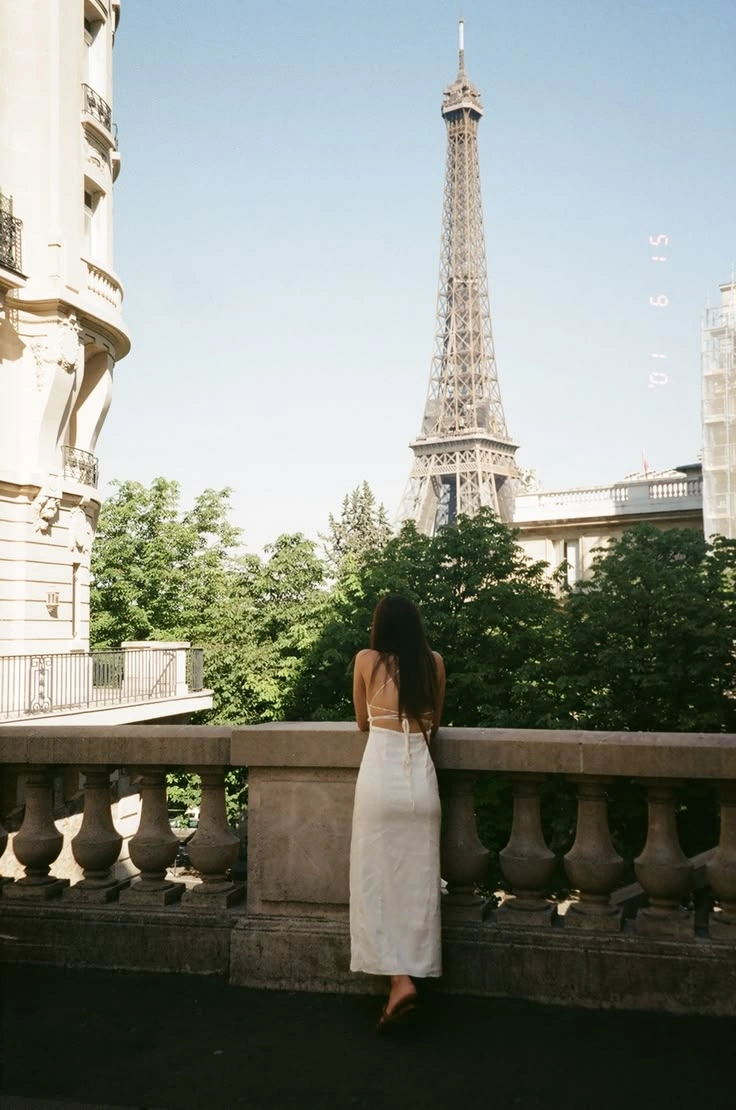 A woman in white overlooking the Eiffel Tower from a Paris balcony